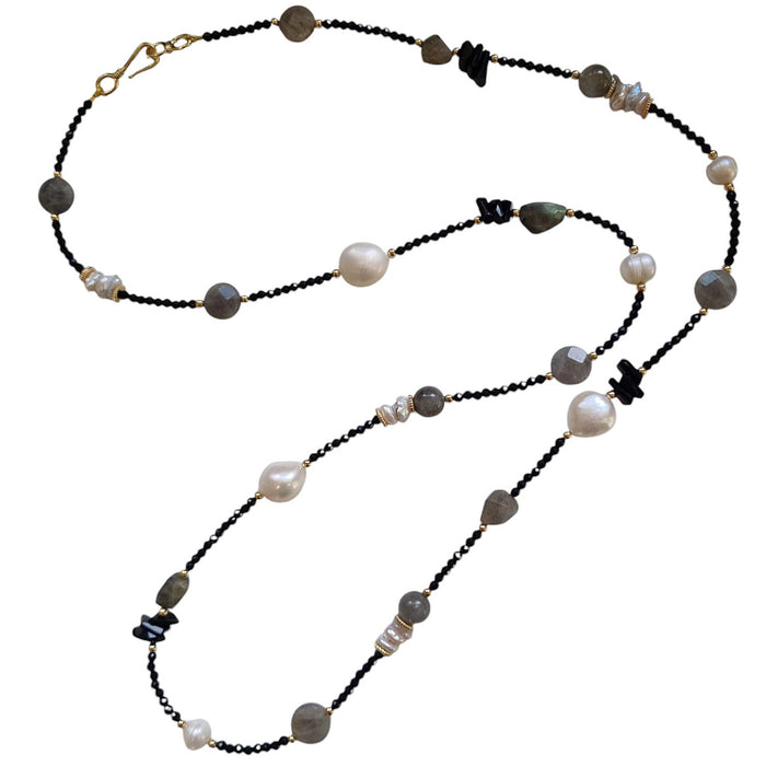 A long necklace featuring a variety of faceted black crystals, pearls, and labradorite stones with a gold-filled clasp.
