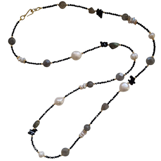 A long necklace featuring a variety of faceted black crystals, pearls, and labradorite stones with a gold-filled clasp.